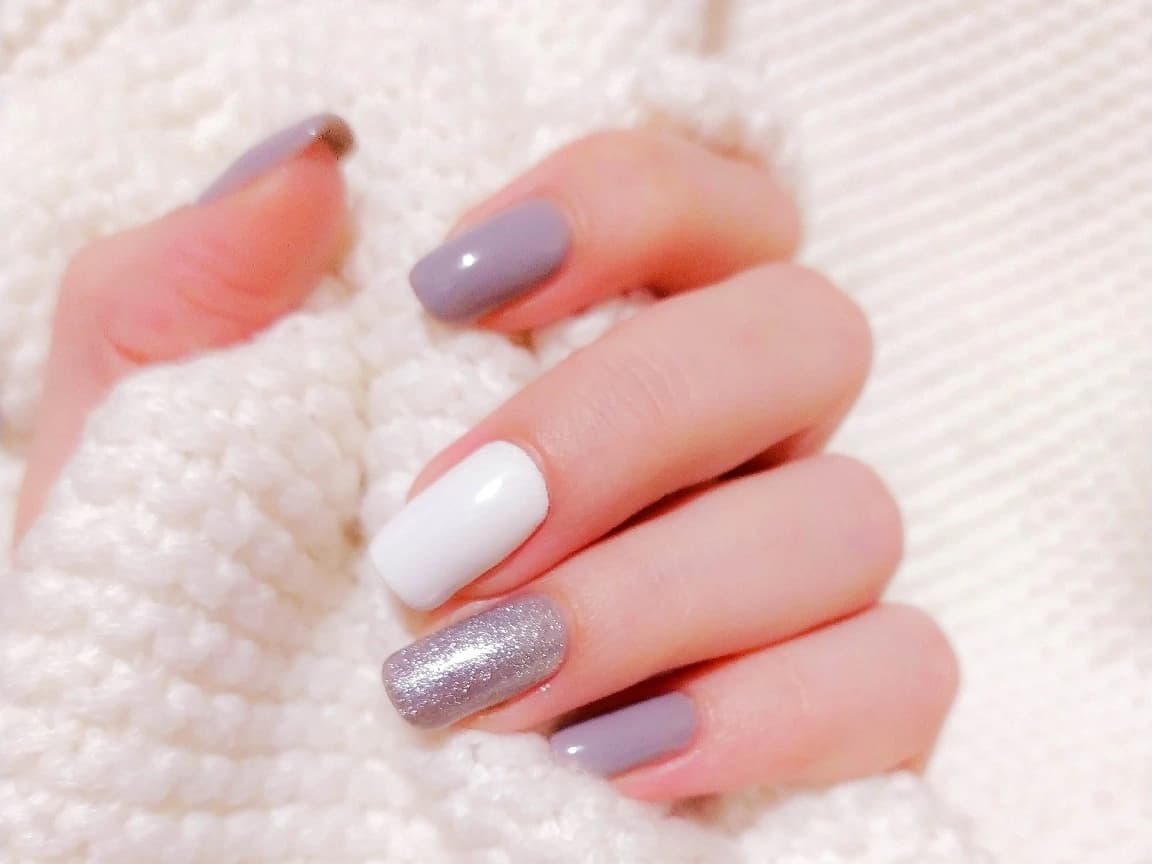 Maniküre in Grau, Weiß und Silber auf einer weißen Strickdecke