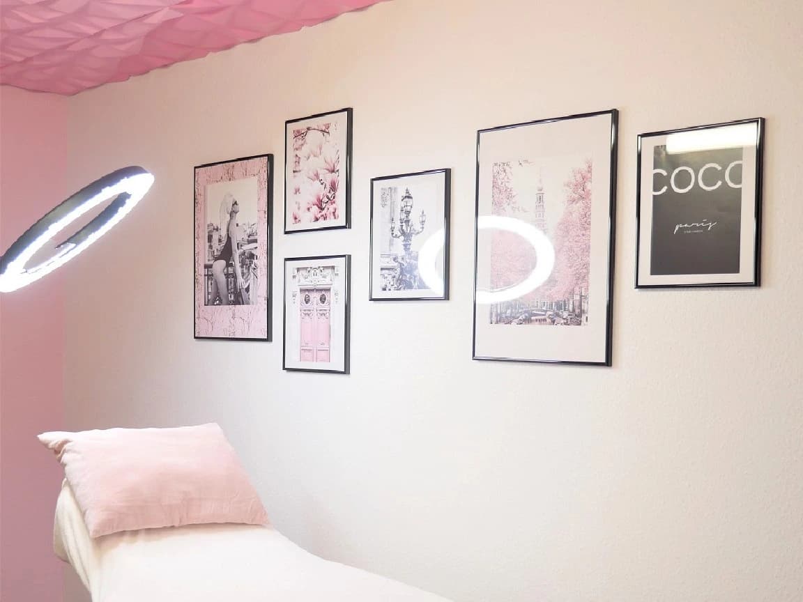 Behandlungsliege mit rosa Kissen unter einer Bilderwand